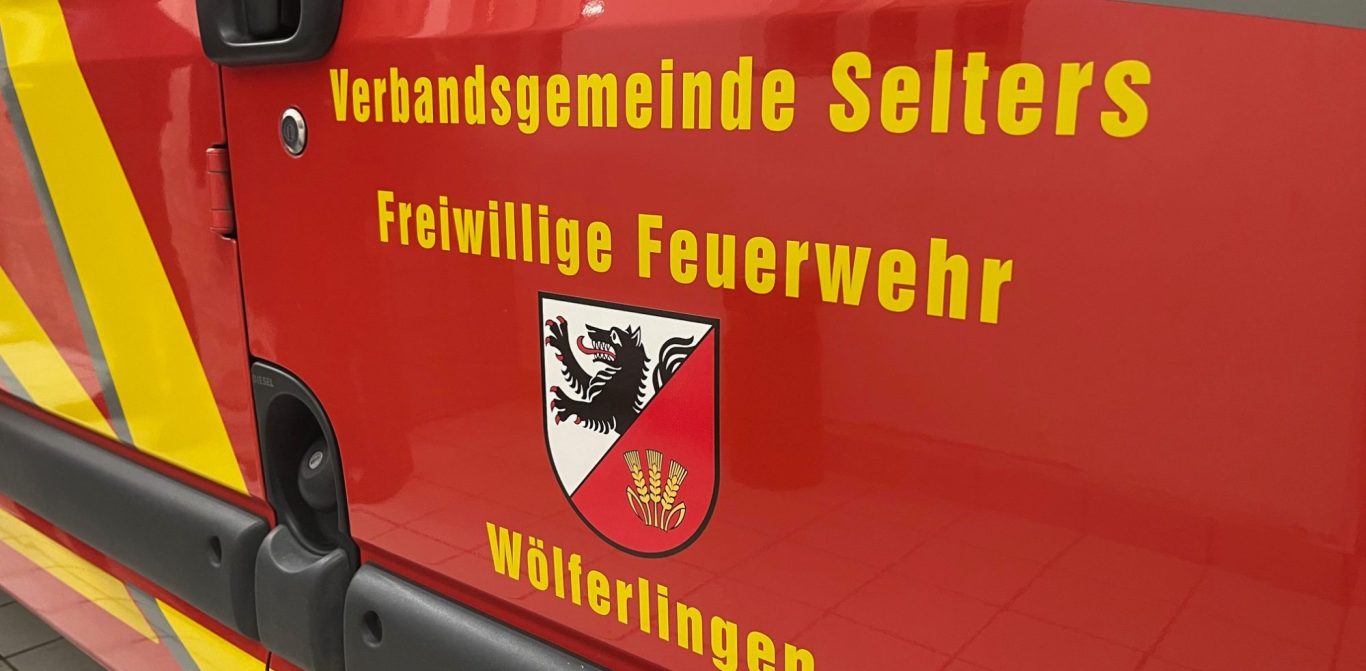 Rotes Feuerwehrfahrzeug steht auf einem Waldweg, umgeben von Bäumen.